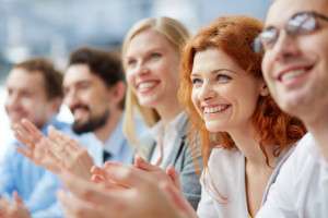 Photo of happy business people applauding at conference, focus on smiling female